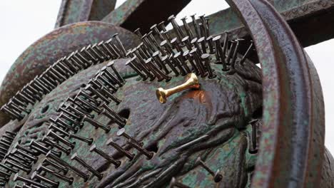 close-up of a metal sculpture with nails and a gold pin