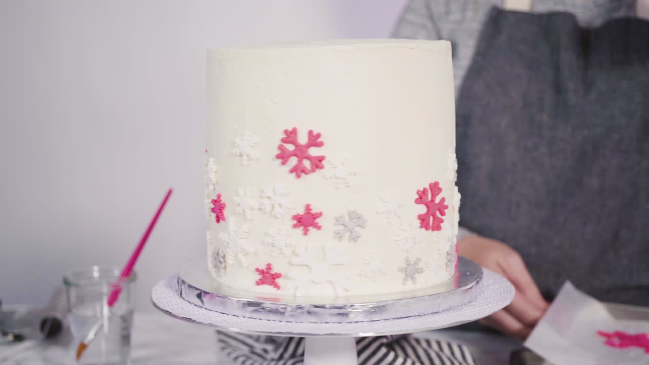 Decorating round funfetti cake with pink and white fondant snowflakes.