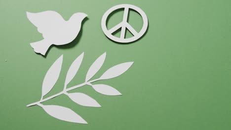 close up of white dove with peace sign and leaf and copy space on green background