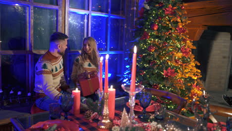romantic couple on christmas background. young man kisses his girlfriend in festive room with candles on the table. new year celebration.