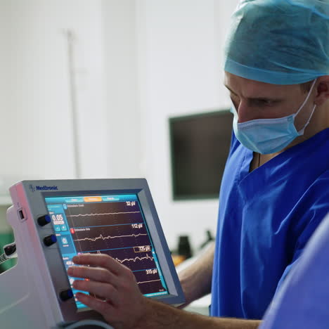 male medic standing near the modern medical equipment in the surgery room. doctor pressing the keys on the touch screen of machine.