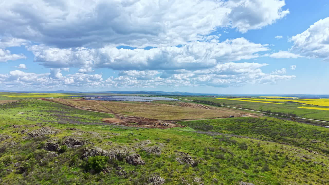 A instalação de painéis solares está sendo realizada em um grande campo com céus claros e colinas distantes.
