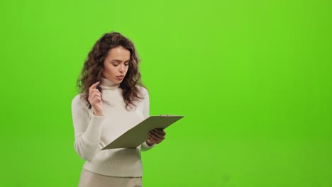 the woman is standing and looking at the camera. she is making notes in the document. she's focused. she is standing on a green background. green screen. 4k.