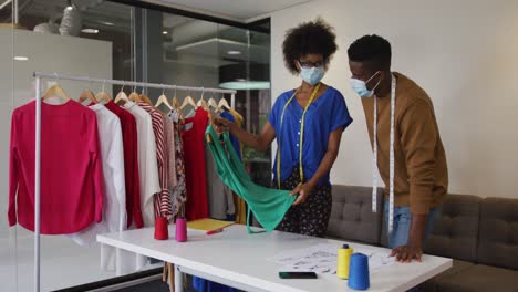 African-american-male-and-female-fashion-designers-wearing-face-masks-in-discussion-at-work