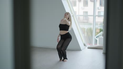 fit girl in black clothes performing contemporary. female dancer shows flowing motions, body and hands waves at white room. modern ballet dance choreography. young woman is moving smoothly