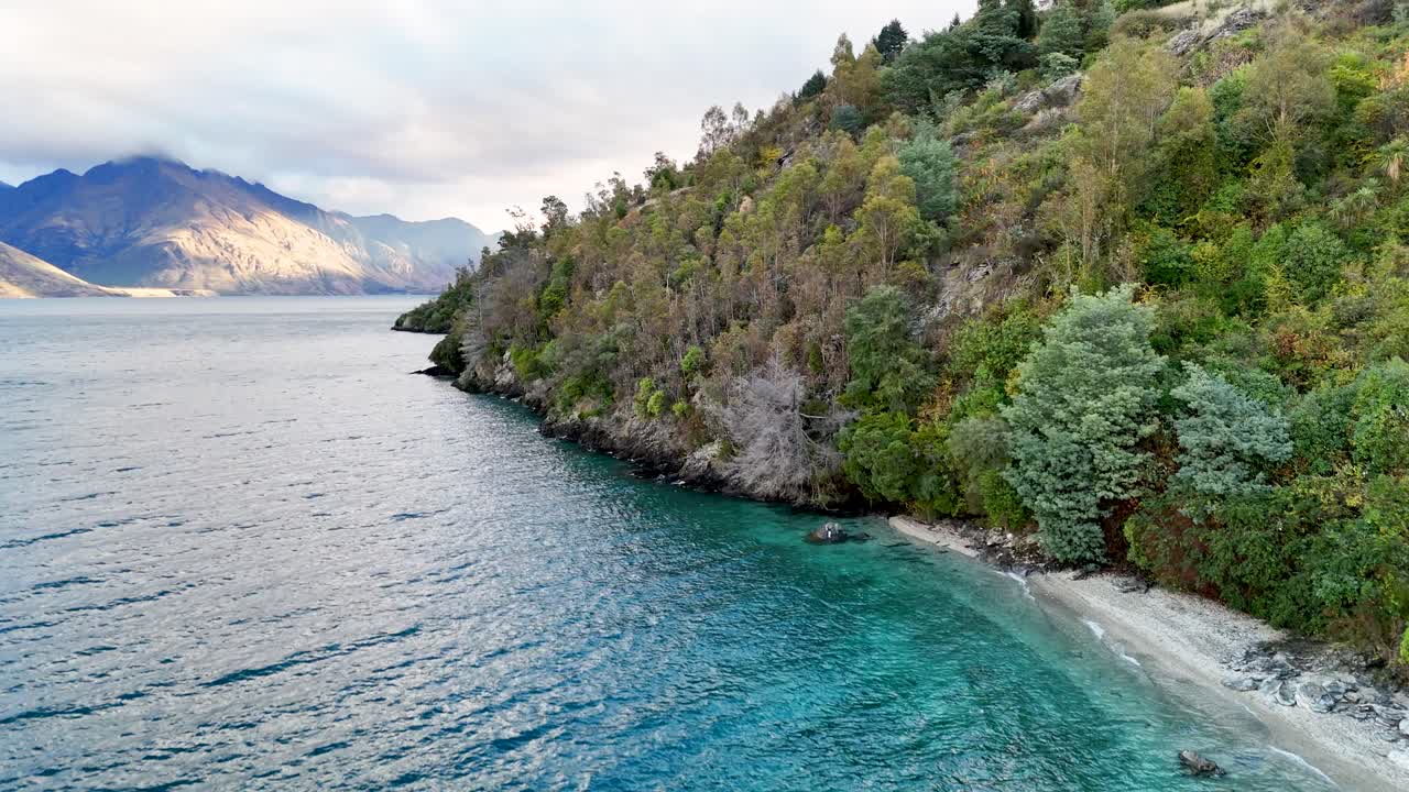 Aerial footage captures Lake Wakatipu's serene waters and lush shoreline in Queenstown, New Zealand, under soft daylight