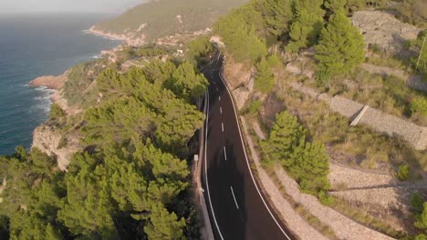 Imágenes-Aéreas-De-La-Carretera-Entre-Las-Montañas-Y-El-Mar-Con-Una-Hermosa-Puesta-De-Sol