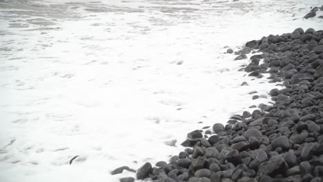 Close-up-of-Winter-Tide-foaming-in-over-rocky-beach-at-Dunraven-Bay,-South-Wales