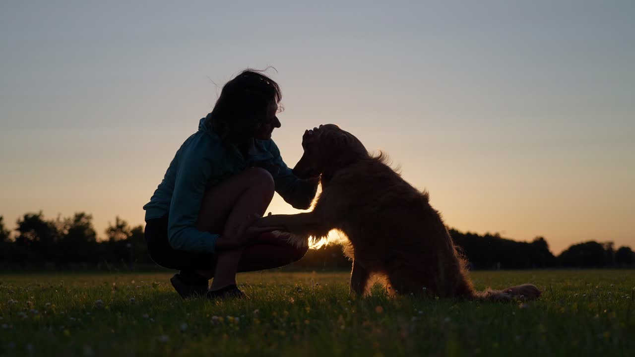 Woman kneeling and petting a golden retriever during sunset in a serene moment
