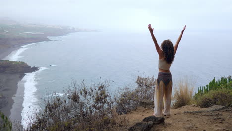 amidst the breathtaking scenery of the ocean, beach, and rocky mountains, a woman practices yoga's warrior pose, embodying motivation and inspiration in her fitness journey