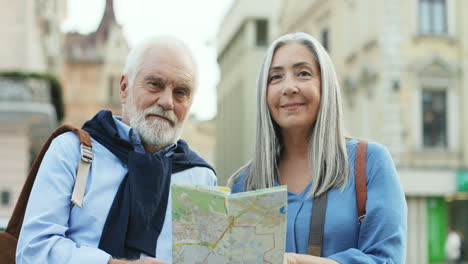 portrait of a senior couple of tourists standing in the city and looking at a map, then smiling to the camera