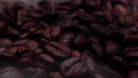 zooming in close up shot of roasted coffee beans with smoke wafting down onto them