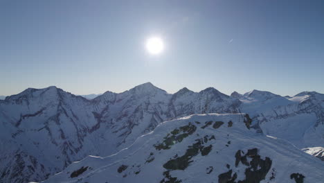 drone flies around snowy mountain peak in austria on which there is a large cross and behind it is a huge snow-covered mountain area