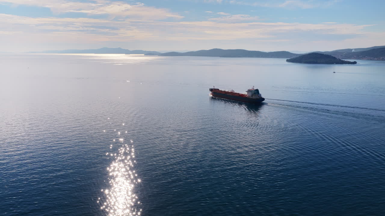 Aerial drone view of an oil tanker traveling across open Adriatic waters with distant mountain ridges and coastal towns visible on the horizon