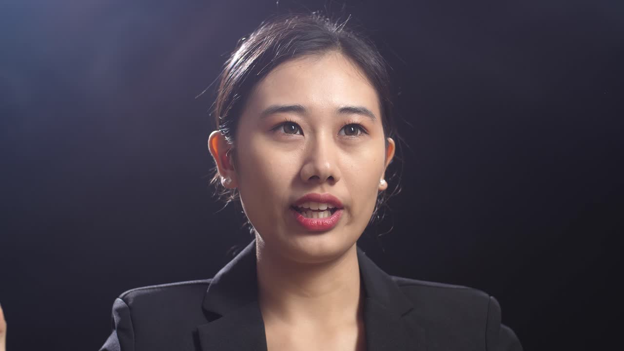 블랙 스크린 스튜디오에서 말하는 비즈니스 슈트를 입은 아시아 스피커 여성의 클로즈업