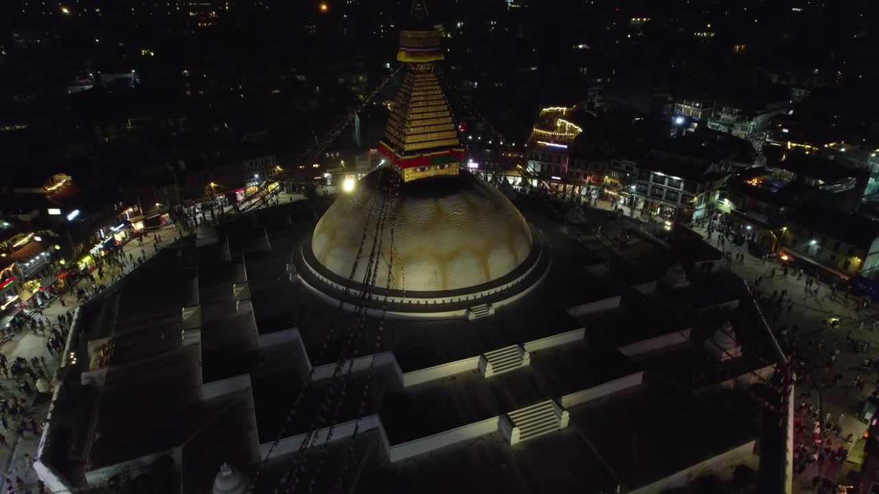 Una ripresa aerea notturna e serena dello stupa di Boudhanath, noto anche come Boudha Nath, che risplende su Kathmandu. Il sacro punto di riferimento buddista si erge radioso sullo sfondo del tranquillo paesaggio urbano notturno.