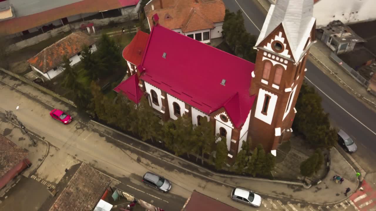 un dron aéreo se acerca y sobrevuela la iglesia de techo rojo en un pequeño pueblo comunitario en la provincia de rumania