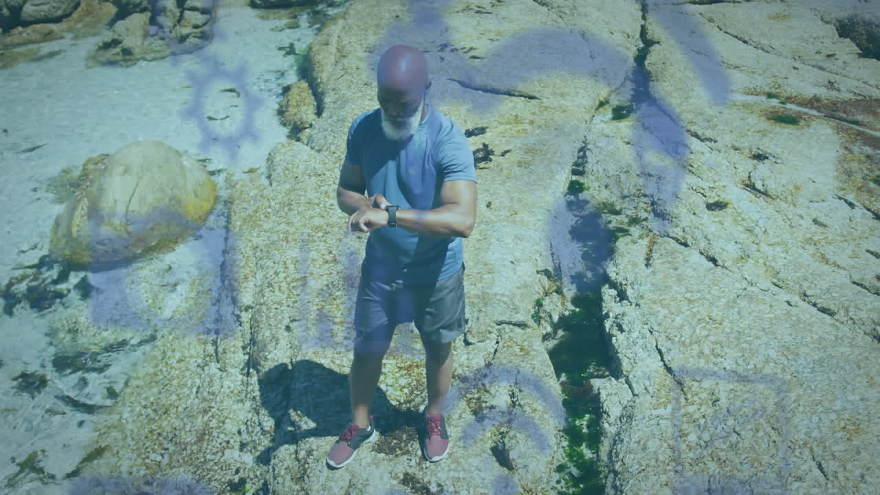 animación de iconos de los medios sobre un hombre afroamericano mayor que usa un reloj inteligente en la playa