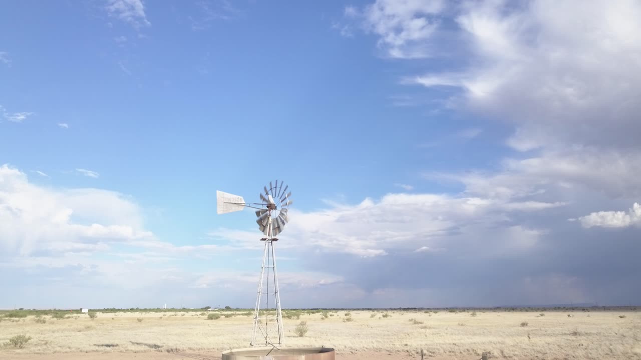 Drone — low angle, slowly moving across the landscape with windmill and skies in background, Texas