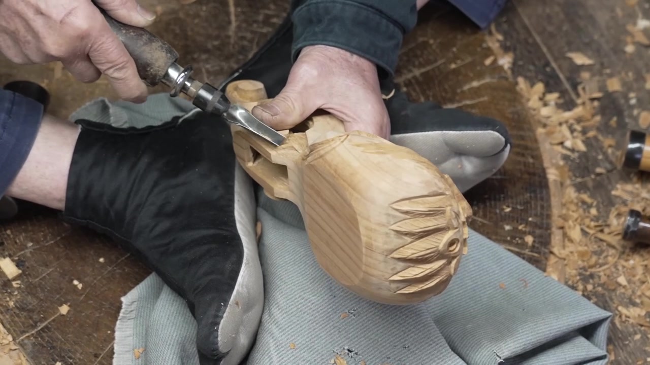 Artigiano che intaglia scaglie decorative in una forma di legno appoggiata su una superficie di lavoro ricavata da un tronco d'albero