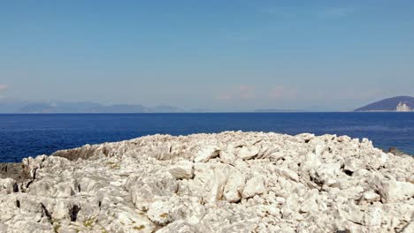 White-Stony-Surface-Of-Paralia-Emplisi-Beach,-Kefalonia-In-Greece-Facing-The-Endless-Blue-Ocean-Waters--Forward-Aerial