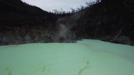 Aerial-dolly-shot-of-the-White-Crater-Kawah-Putih-known-for-geothermal-activities-and-volcanic-atmosphere-with-milky-turquoise-waters-during-an-exciting-transit-in-Bandung-Indonesia