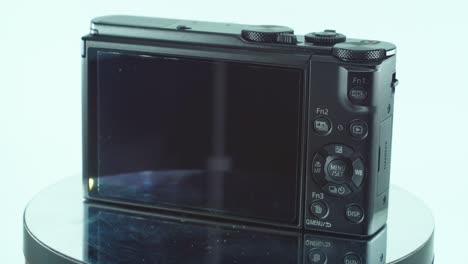 Close-up-shot-of-a-small-black-pocket-camera,-aluminiaum-built,-function-buttons,-lights-reflecting-on-the-screen,-on-a-360-rotating-stand,-slow-motion,-4K-video