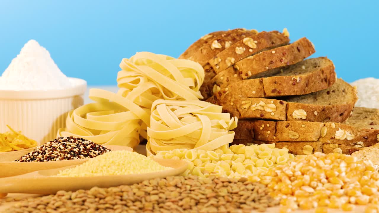 A variety of grains and sliced bread arranged on a table with a vibrant blue backdrop, showcasing diverse textures and colors