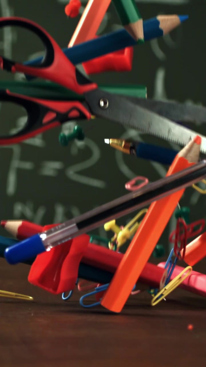 Colorful School Supplies Falling onto a Desk in Front of a Chalkboard