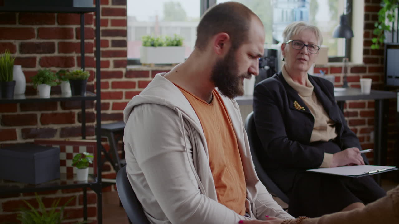 Frustrated man sharing story with group of people and therapist at aa therapy meeting