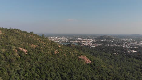 Toma-Aérea-Lenta-Hacia-Adelante-De-Una-Montaña-Cubierta-De-Maleza-Con-La-Hermosa-Ciudad-De-Tiruvannamalai-En-El-Fondo