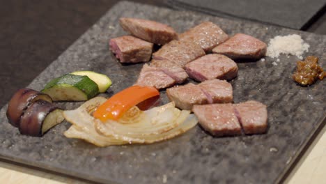 Plato-De-Carne-Japonés-Kobe-Wagyu-Que-Sirve-Con-Rodajas-De-Berenjena,-Pimientos,-Cebolla,-Calabacín,-Sal,-Pimienta-En-Un-Plato-Tradicional-De-Piedra,-Restaurante-Japonés