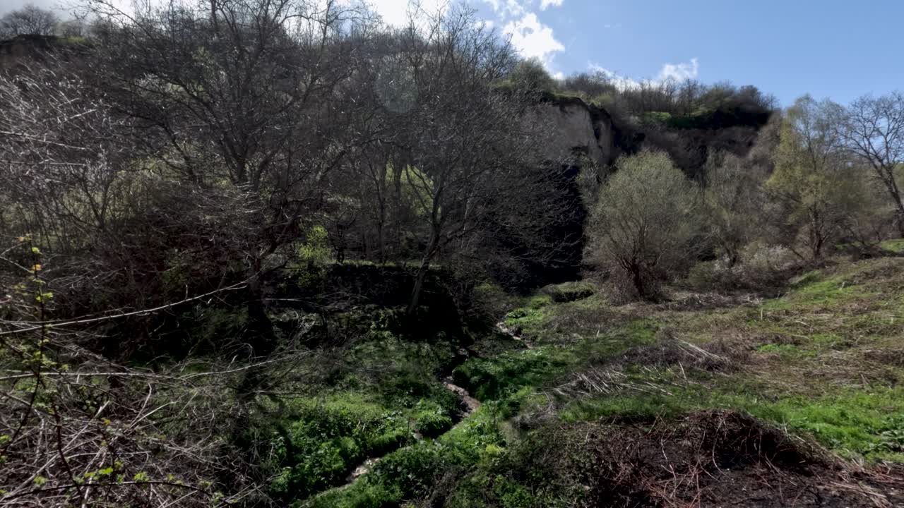 I visitatori esplorano una valle verde caratterizzata da alte scogliere e alberi. Un piccolo ruscello scorre attraverso l'area, con nuvole in alto e la luce del giorno che illumina il paesaggio.