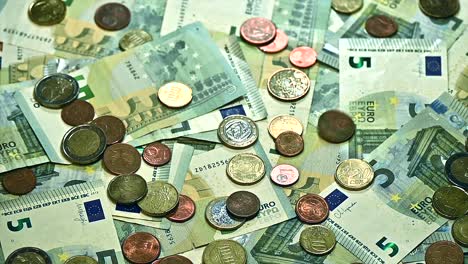 shower of euro coins raining onto a pile of five euro bills on a table, close-up perspective