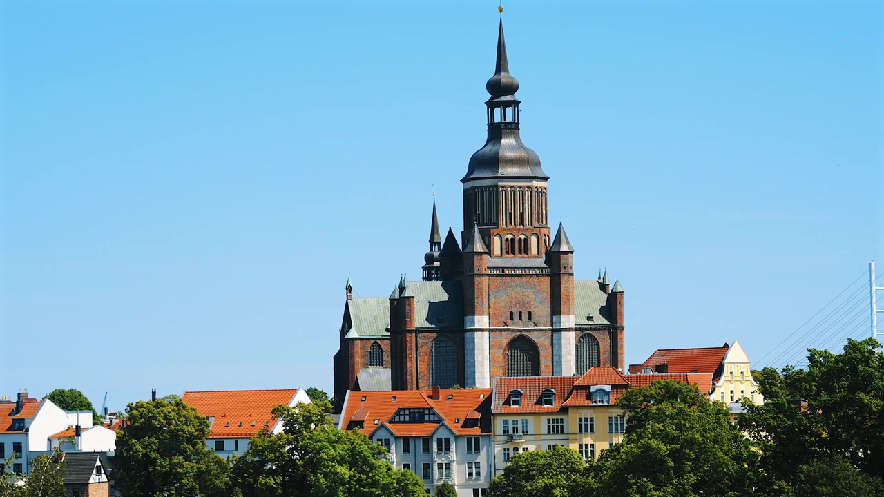 Gereja St. Mary menjulang di atas kota tua beratap merah Stralsund, Jerman, sebuah gereja Gotik bata besar dengan menara berkubah barok dengan latar langit biru cerah pada hari musim panas yang cerah