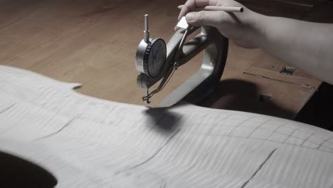 stringed instrument maker master luthier proceed with graduation work in cello back plate, use thickness gauge caliper, measure levels, use pencil write values on wood , cremona, italy workshop