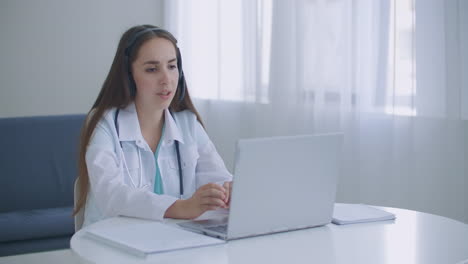 Der-Arzt-Trägt-Ein-Headset-Und-Konsultiert-Eine-Patientin.-Führen-Sie-Einen-Online-Webcam-Videoanruf-Auf-Dem-Laptop-Bildschirm-Durch.-Telemedizin-Videokonferenz,-Remote-Computer-App,-Virtuelles-Treffen.