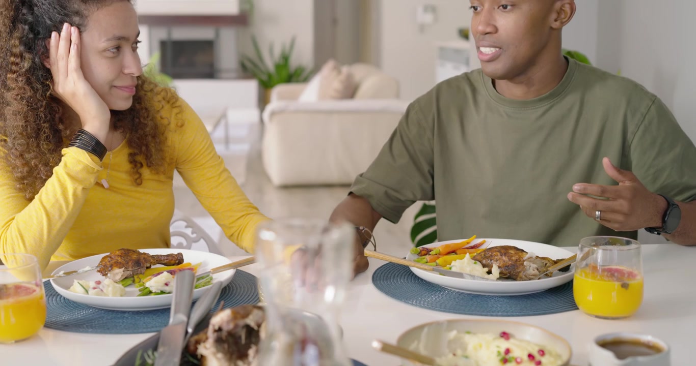 Couple se tenant la main à table, tandis qu'un homme afro-américain parle, discutant d'un rôti.