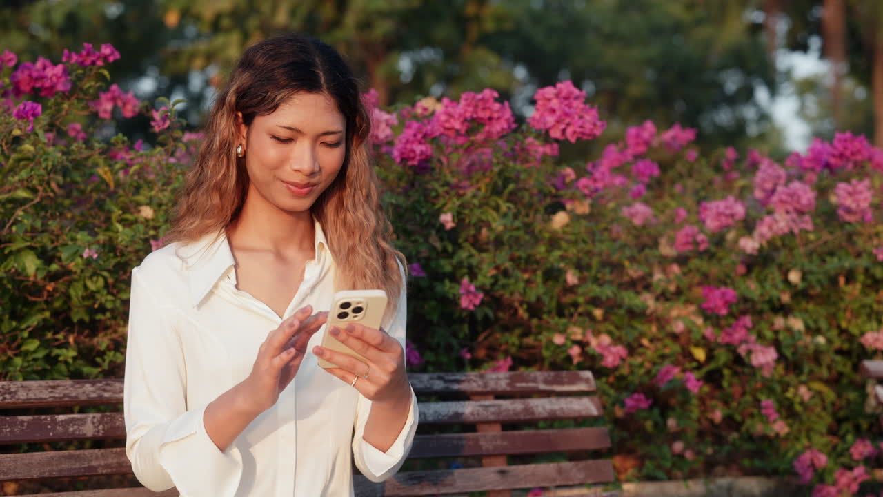 Young Woman Using Smartphone in a Park with Pink Flowers