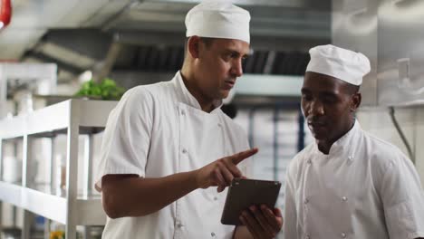 two diverse male chefs talking and using tablet in restaurant kitchen