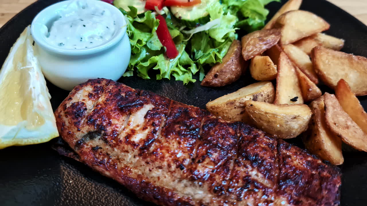 Grilled chicken fillet with potato wedges, salad, sauce and lemon wedge