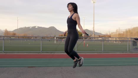 Tiro-Circular-De-Cardán-De-Mujer-Asiática-En-Ropa-De-Entrenamiento-Saltando-La-Cuerda-Al-Aire-Libre