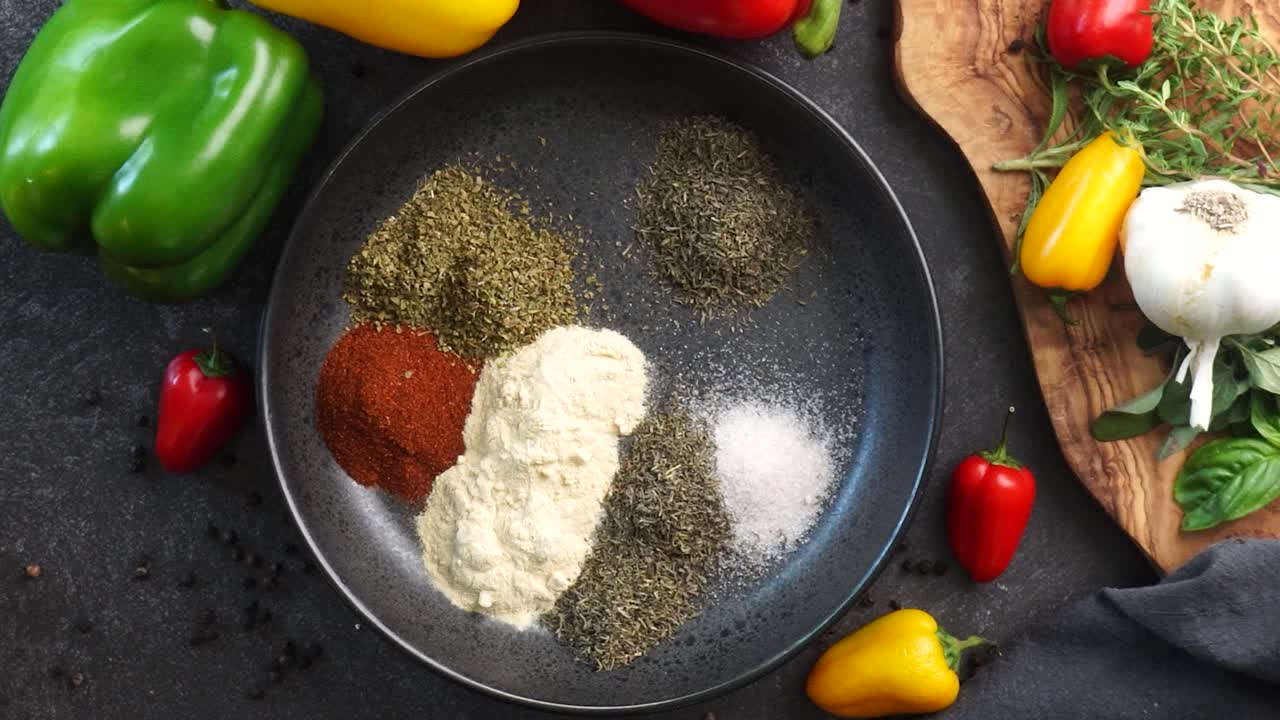 Making a vibrant Cajun Spice Blend, mixing red paprika, cayenne pepper, oregano, thyme, white garlic onion powder and black pepper in a bowl, creating a striking contrast against a black background.