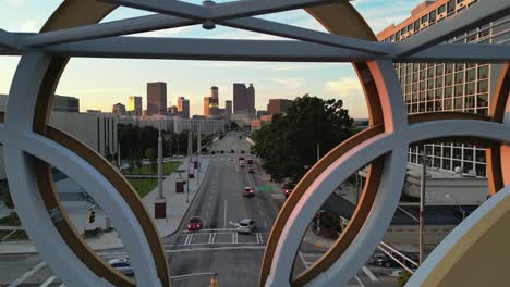 Aerial-backwards-shot-showing-Olympic-rings-on-bridge-and-traffic-on-road-in-front-of-Skyline-during-golden-hour