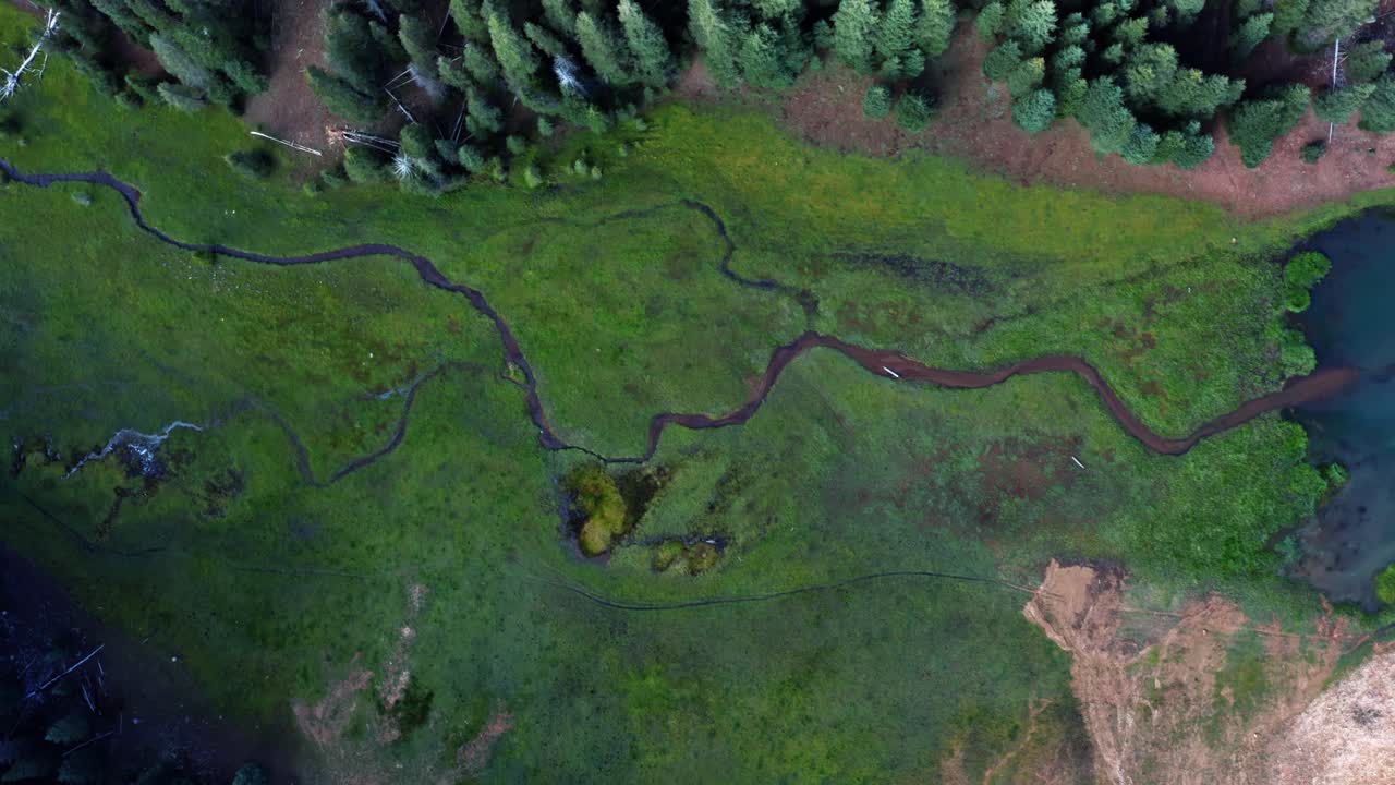 hermoso dron aéreo a vista de pájaro de un pequeño arroyo salvaje rodeado por un campo de hierba que conduce al lago del embalse del prado de anderson hasta el cañón del castor en utah en un cálido día de verano