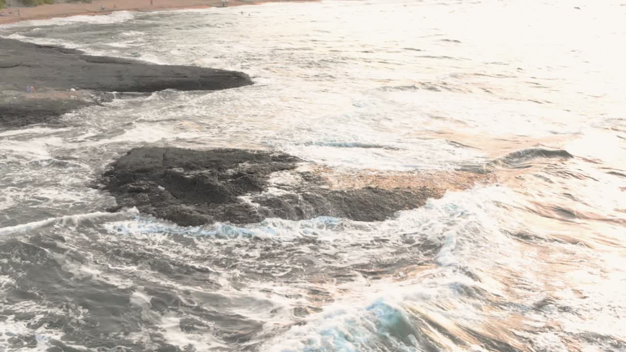 Drone slow motion footage of rock in the sea close to the seashore, waves wash over the cliff