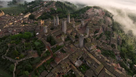 Vista-Aérea-De-Drones-De-Torres-En-El-Casco-Antiguo-De-San-Gimignano-Durante-La-Mañana-Brumosa-En-La-Provincia-De-Siena,-Toscana,-Italia