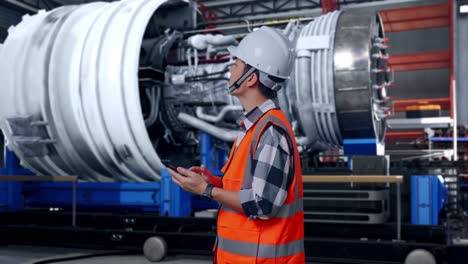 side view of asian male engineer with safety helmet using smartphone and looking around while standing with airplane engine maintenance conducted, analytics checking the turbine