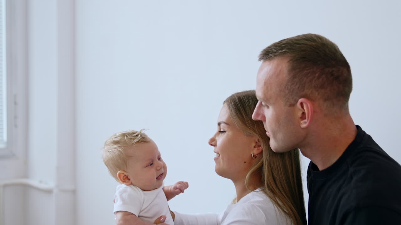 Mom and dad with their infant at home. Mother holds her lovely baby and kid smiles to parents.