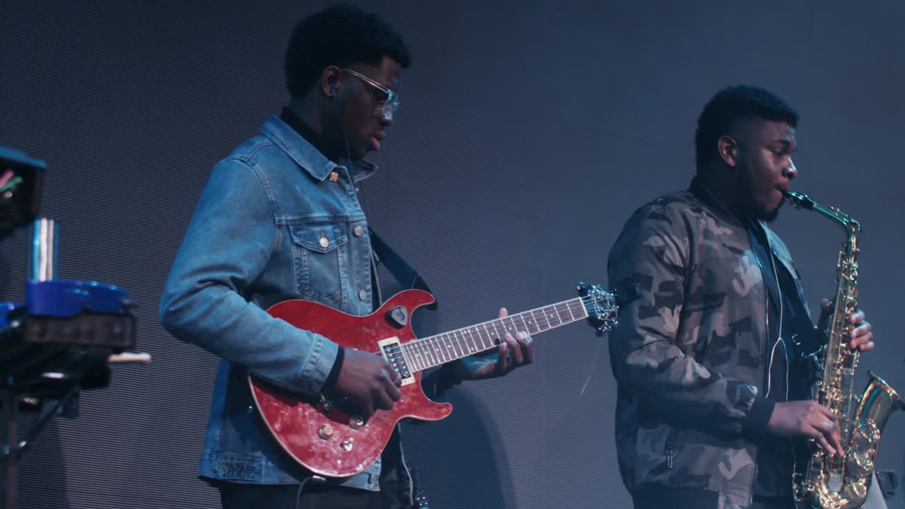 Two African American men play musical instruments while standing on the stage